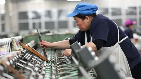 Women's psychologists apply in the Spin Ship Sumination line in the Chinese factory. Wearing a blue cap with white apron over his blue uniform. 